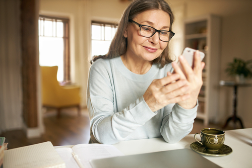 A woman with glasses gazes pleasantly at her smartphone.