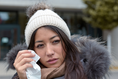 woman wearing winter hat and jacket while using tissue to wipe her eyes