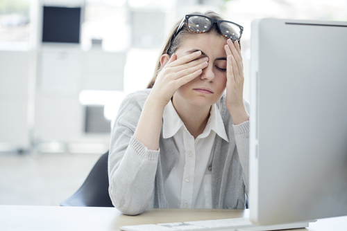woman sitting in front of computer while rubbing her eyes